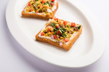Bread ppadi chaat/chat is a yummy starter/appetizer from India, served in a plate garnished with tomato, sev and coriander and masala. selective focus