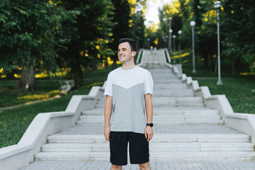 Joyful young man si listening to the music and smiling in park.