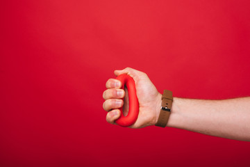 A man&amp;amp;#039;s hand holding and pressing a red rubber ring or hand gripper on red background .