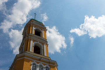 Yellow Orthodox Christian church with a green dome in summer against a blue sky with white clouds.