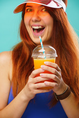 Woman wearing a blue swimsuit and hat drinks fruit juice from a cup