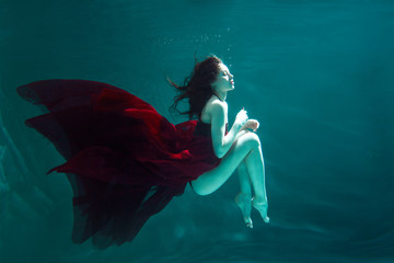 Mystical underwater portrait of a beautiful young woman in a red dress. Girl swimming underwater
