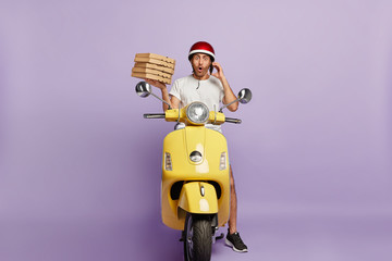 Food delivery concept. Shocked courier takes order over phone from customer, holds stack of cardboad pizza boxes, stops to have break drives fast motorbike, astonished to loose way, doesnt know route