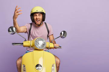 Irritated impatient guy works in delivery service, annoyed with traffic jam on road, raises hand in...