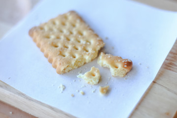 Dry cracker cookies crumb with white paper on wooden plate.