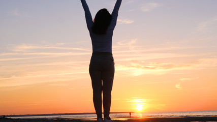 A young woman on the background of the sunset the sun on the seashore does exercises exercised by...