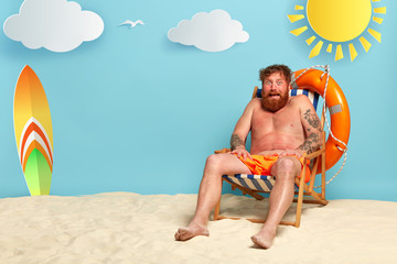 Frightened bearded redhead man gets sunburned at comfortable beach chair, has , needs protective...