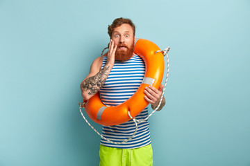 Beach safeguard man in sailor vest and green shorts, works at sea resort, has stupefied facial...