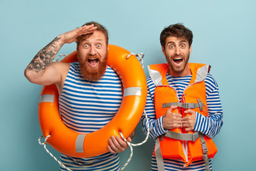 Two male lifeguards keep beach safe in summertime period, gaze into distance with happy...