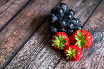 Fresh Scottish strawberries and black grapes on top of wooden table.