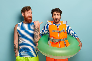 Smiling redhead bearded young man points at friend coward, gives lesson of swimming, spend leisure...