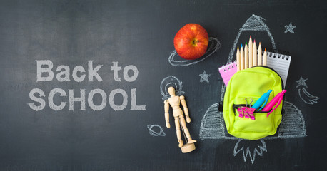 Back to school concept with small bag backpack, school supplies and rocket sketch over chalkboad...