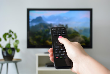 Watching TV. A woman's hand holding the TV remote control with a television in the background....