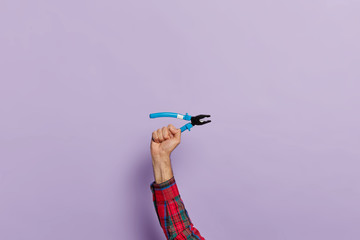 Mans hand holds pliers with blue plastic handles for construction and repair, isolated over purple background. Pointy nose pliers in hands of engineer or handyman. Hand tool. Symbol of hard work