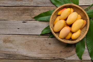 Mango fruit in basket and green leaf on wooden background, top view