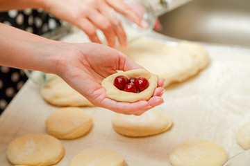 Cooking cherry pies in the home kitchen. Women's hands in the process of cooking cakes with cherries.