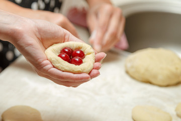 Cooking cherry pies in the home kitchen. Women's hands in the process of cooking cakes with cherries. © Andrii