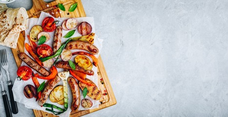 Grilled vegetables and sausages on wooden board,