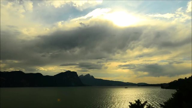 Magnificent panorama of mountains and lake in central Switzerland. Setting sun painted the clouds in the grand color. Time lapse.