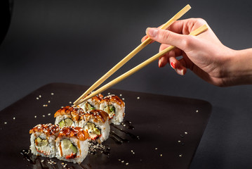 Hand with chopsticks for sushi taking a roll on dark background © rostyslav84
