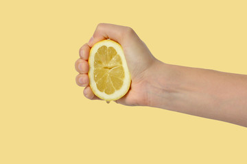 Woman's hand squeezing a lemon isolated on yellow background