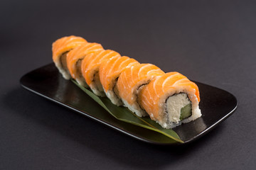 Close up sushi rolls in a black plate on dark background