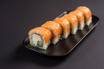 Close up sushi rolls in a black plate on dark background