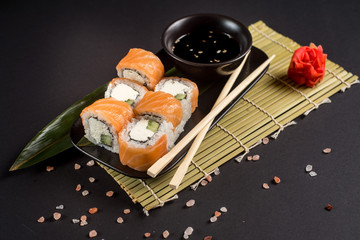 Close up sushi rolls in a black plate on dark background