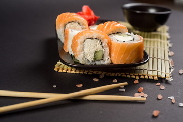 Close up sushi rolls in a black plate on dark background