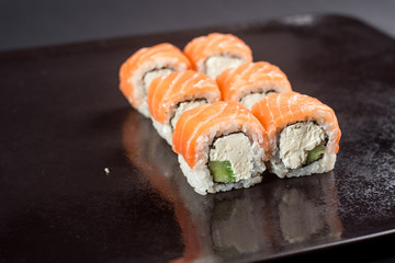 Close up sushi rolls in a black plate on dark background
