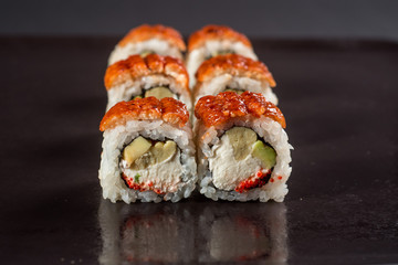 Close up sushi rolls in a black plate on dark background