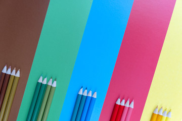 Creative flat lay back to school concept with colored pencils on blue, brown, green, red and yellow background. Minimal concept art. Top view, copy space.