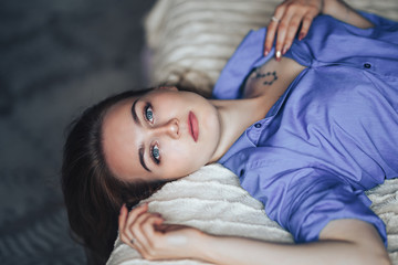 Sexy young beautiful woman with blue big eyes lond hair lying on bed at home in blue shirt