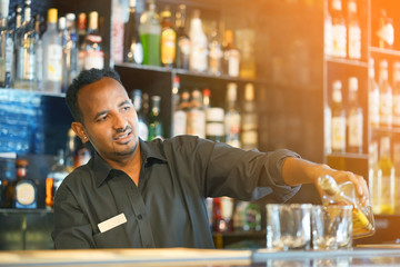 African bartender man pours whiskey to the client of the hotel bar. The concept of service. Focus on the bartender. Toning.