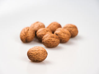 One walnut (Júglans régia) close-up in focus on a white background, behind there are still many nuts in the out-of-focus.