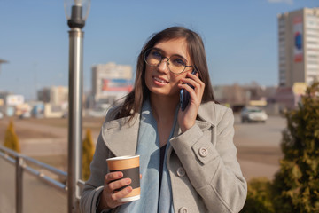 Young beautiful woman talking on the mobile phone and drinking coffee in the street