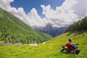 Fototapeta premium Hiker sitting in the meadow admires the mountain panorama in front of him.