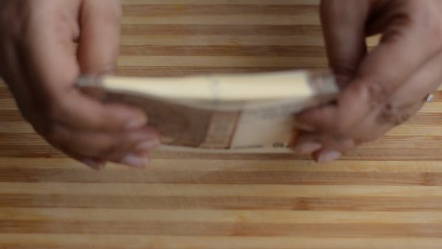 Hands counting new brown Rs10 Indian Rupees Currency notes against a wooden board background and arranging them