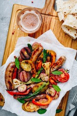 Grilled vegetables and sausages on wooden board