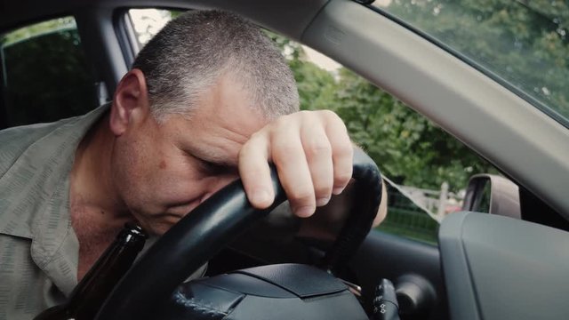Drunk driver with a bottle of alcohol in his hand dozing on the steering wheel