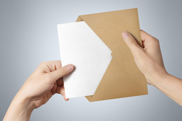 Fototapeta premium Hands pulling a blank paper out of a brown envelope on gray background