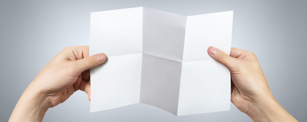 Obraz premium Hands holding a folded sheet of white paper on gray background