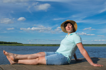 Fototapeta na wymiar close-up, woman in a hat on a pier, is resting and enjoying a beautiful sky and lake