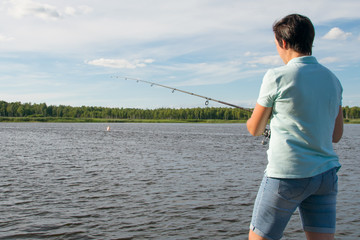 close-up, woman on the background of a beautiful lake and blue sky, fishing with a fishing rod, rear view