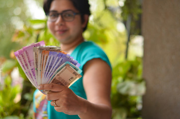 An Indian women holding all the colorful new released Indian Rupees currency notes after demonetisation in denominations 10,50,100, 200, 500, 2000 in her hands with her blur face in the background
