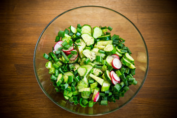 fresh salad of cucumbers and greens in a plate on a wooden