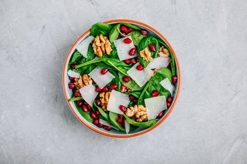 Spinach salad bowl with pomegranate seeds, walnuts and cheese slices.