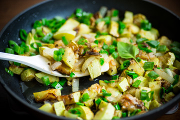 zucchini fried with onions and herbs in a pan on a wooden table