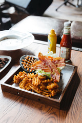 Charcoal cheese burger with crunchy bacon, cabbage, onion, tomato, thousand island sauce and waffle fries. Served with ketchup and mustard on wooden table.