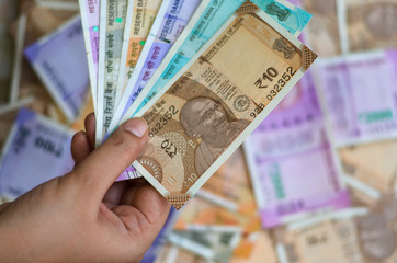 Closeup of brand new colorful Indian currency bank notes of 10, 50, 100, 200, 500 and 2000 rupees bundle issued and in circulation after demonetisation held with hand with many notes in the background